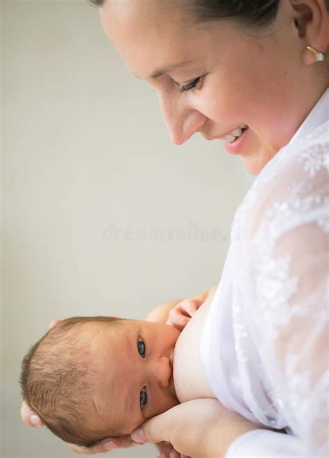 Mom Feeds Newborn Standing In A White Interior Breast Feeding Stock