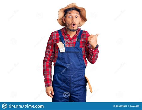 Handsome Latin American Young Man Weaing Handyman Uniform Surprised Pointing With Hand Finger To