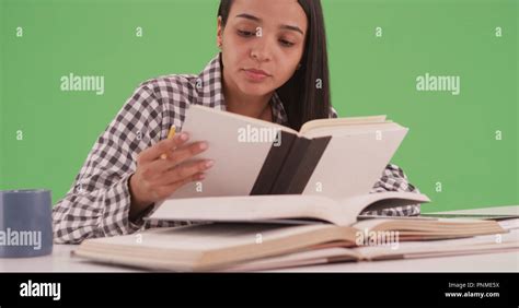 Hispanic College Student Studying For A Final With Many Books On Green