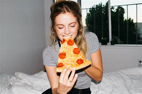 Young Woman Eating Slice Of Pepperoni Pizza On Bed In Apartment By Stocksy Contributor Jesse