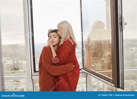 Portrait Of Attractive Lesbian Couple In Love Wearing Red Clothes Hugging Near Opened Window