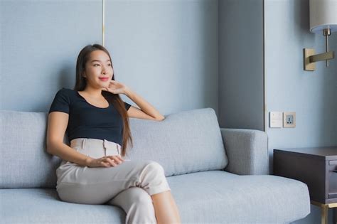 retrato joven y bella mujer asiática sentarse en el sofá relajarse en la sala de estar foto gratis
