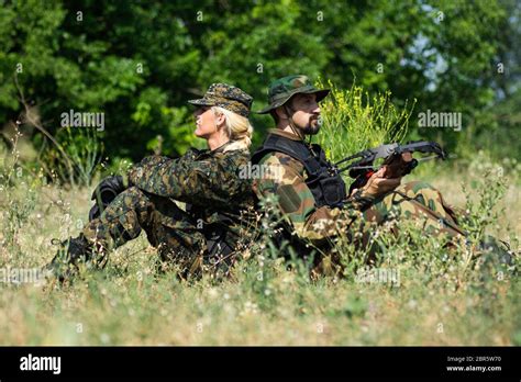 The Female And Male Soldiers In Different Military Uniforms Are Sitting Down In Grass In Nature