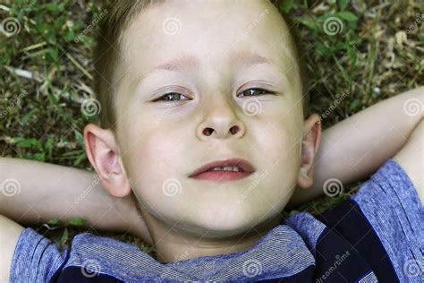 Portrait Of Cute Boy Lying Back On The Grass With His Hands Behind His