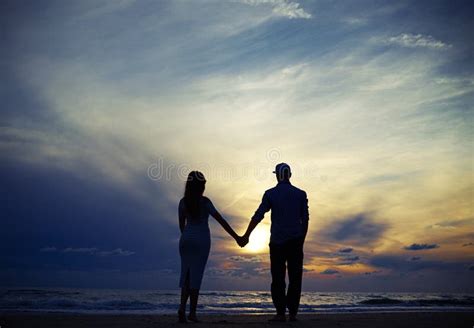 Romantic Couple Holding Hands While Looking To The Sunset Stock Photo