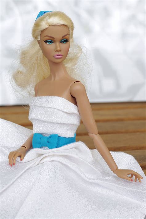 A Barbie Doll Sitting On Top Of A Bed Wearing A White Dress And Blue Bow