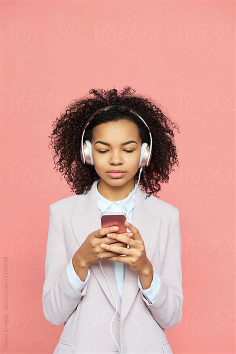 portrait of trendy black girl in classic pink jacket standing with smartphone and headphones on