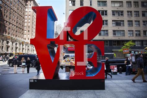 A Large Red Love Sculpture On The Side Of A Road In Front Of Tall Buildings