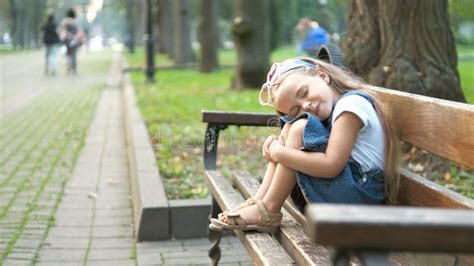 Small Tired Child Girl Sitting On A Bench With Closed Eyes Resting In