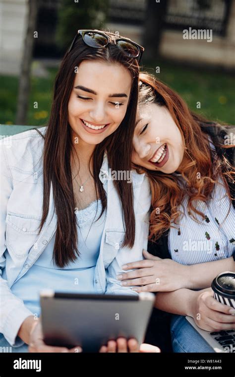 Two Beautiful Woman Having Fun Laughing While Holding A Tablet Sitting
