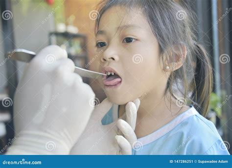 asian doctor in surgical gown examining a little cute asian patient girl with throat sick in