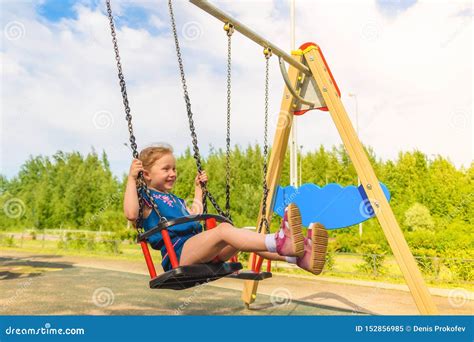 Happy Little Child Girl Laughing And Swinging On A Swing In The City