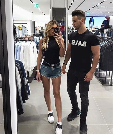 A Man And Woman Walking Through A Clothing Store Talking On Their Cell Phones While Holding Hands