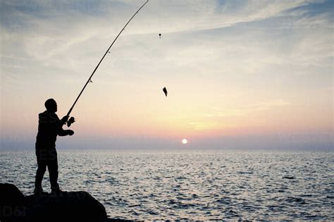 Silhouette Of Man Fishing At Sunset Stock Photo
