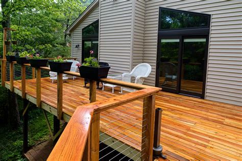 A Wooden Deck In Front Of A House With White Chairs And Plants On The
