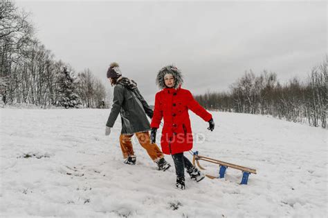 Teenage Girl Pulling Sled While Small Girl Walking On Snow During