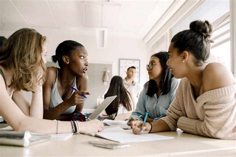 Female Teenagers Discussing While Sitting By Table In Classroom Stock Photo