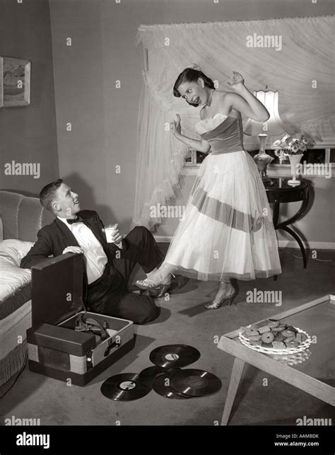 1950s 1960s Teenie Paar Im Wohnzimmer In Prom Kleid And Smoking Kerl Sitzt Am Boden And MÄdchen