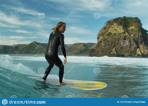 A Young Male Surfer In A Black Wetsuit Rides A Longboard Surfboard On A