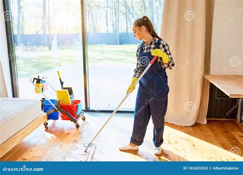 Female Maid In Blue Uniform Cleaning Floor In Bedroom Stock Image