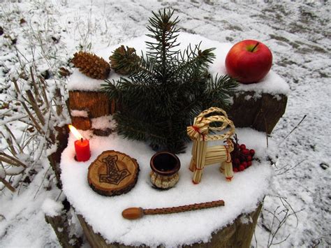 A Small Christmas Tree With Ornaments And Candles On Top Of It In The Snow Next To An Apple
