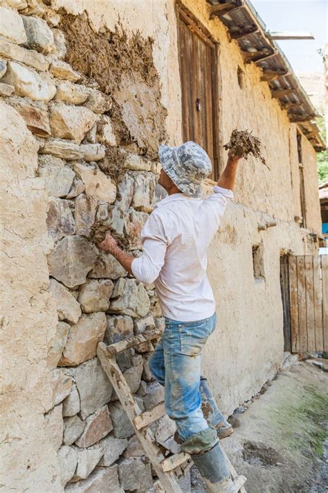 Worker Applying Mud Plaster To A Traditional Stone House Editorial