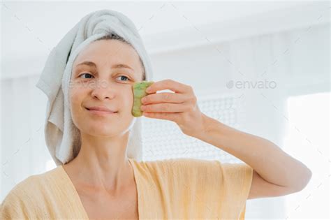 Woman In Bathrobe And A Towel On Her Head Looking In The Mirror And Making Face Massage With