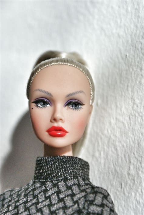 A Close Up Of A Doll Wearing A Dress And Red Lipstick On Her Lips With A White Wall In The