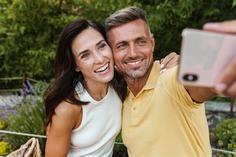 Portrait Of Joyful Middle Aged Couple Taking Selfie Photo On Cellphone And Hugging While Walking