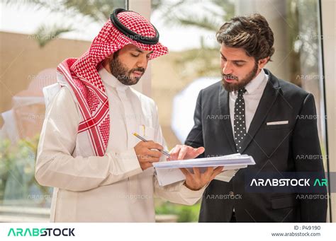 رجل اعمال عربي سعودي خليجي بالثوب السعودي التقليدي يتناقش مع عميل يرتدي البدلة الرسمية، اتفاقية