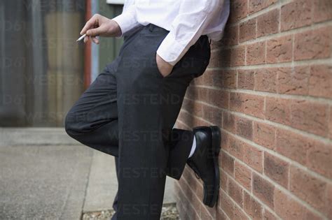 Low Section Of A Businessmen Leaning Against A Wall And Smoking A