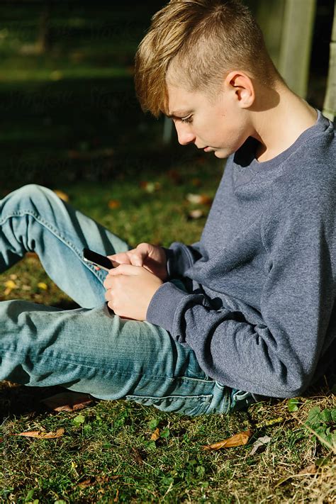 Teenage Boy Using A Mobile Phone Outdoors By Stocksy Contributor