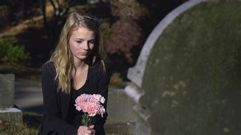 Sad Girl Sitting At Gravestone In Cemetery Holding Pink Flowers 4k
