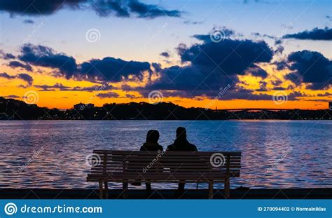 Rear View Of Silhouette Couple Sitting On Bench By Sea Against Sky