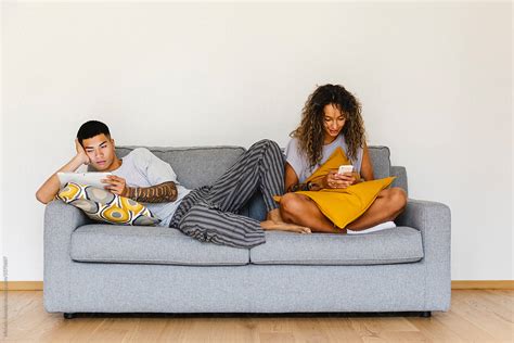 Couple Relaxed On Sofa Looking At Cellphone And Digital Tablet By
