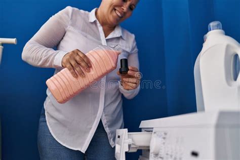 Middle Age Woman Smiling Confident Pouring Detergent At Laundry Room