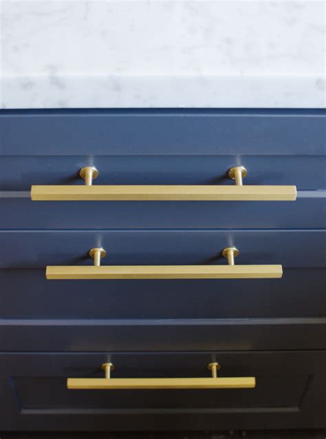A navy blue center kitchen island is lit by gold and white pendant. Top Hardware Styles To Pair With Your Shaker Cabinets