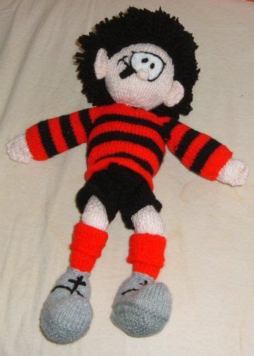 A Knitted Doll Laying On Top Of A White Bed With Red And Black Stripes