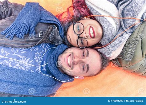 Happy Couple Lying Down Holding Heads Together Looking Up At The Camera