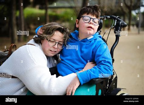 Mother Hugging Her Disabled Son In A Wheelchair While Enjoying The Day Outdoors Together Stock