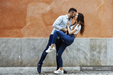 Affectionate Couple In Love Kissing In Front Of A Wall Outdoors