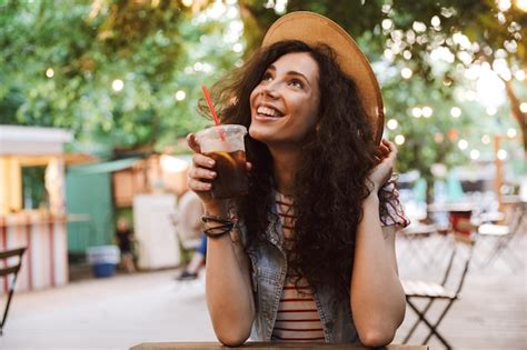 morena adolescente vistiendo sombrero de paja de verano bebiendo té frío de un vaso de plástico