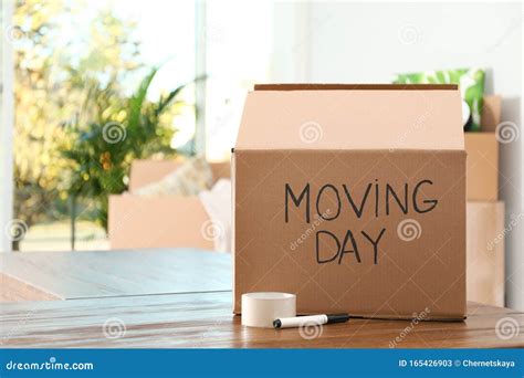 Cardboard Box With Words Moving Day And Packaging Items On Table Stock