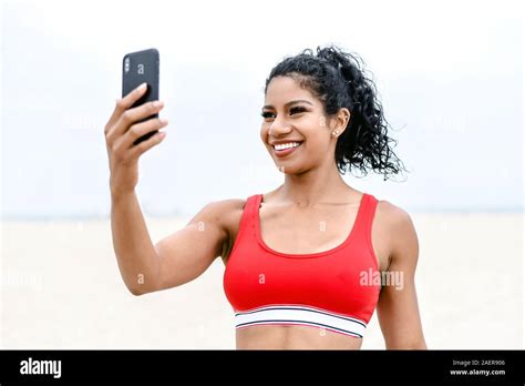 Smiling Latina In Sports Bra Takes Selfie With Smart Phone Stock Photo