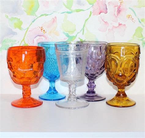 Five Different Colored Glass Goblets Lined Up In A Row On A White Surface