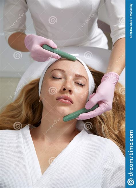 Young Woman Receiving Facial Massage With Stone Sticks In Beauty Salon