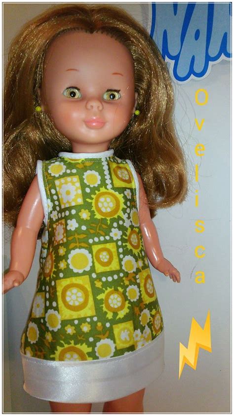 A Doll With Blonde Hair Wearing A Green And Yellow Dress Standing Next