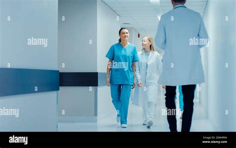 Female Surgeon And Female Doctor Walk Through Hospital Hallway Talking