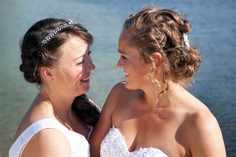 just married happy lesbian couple in white dress near small lake look each other in the eyes