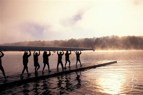 Crew Team Carrying An 8 Man Rowing Scull To Lake In The Early Morning